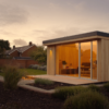 Modern cedar garden sauna cabin with full glass front and warm interior lighting in a UK back garden at dusk