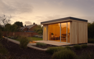 Modern cedar garden sauna cabin with full glass front and warm interior lighting in a UK back garden at dusk