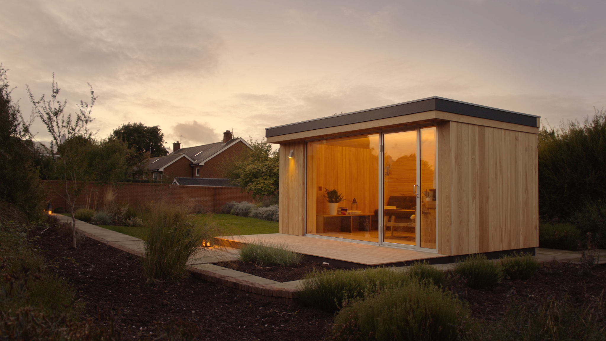 Modern cedar garden sauna cabin with full glass front and warm interior lighting in a UK back garden at dusk