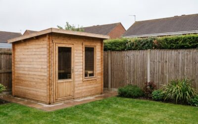 A compact timber cabin sauna on a paved base in a UK suburban back garden, near a timber boundary fence